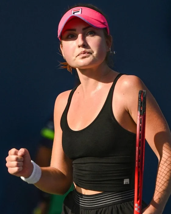 Tennis player in a pink visor pumping her fist between points